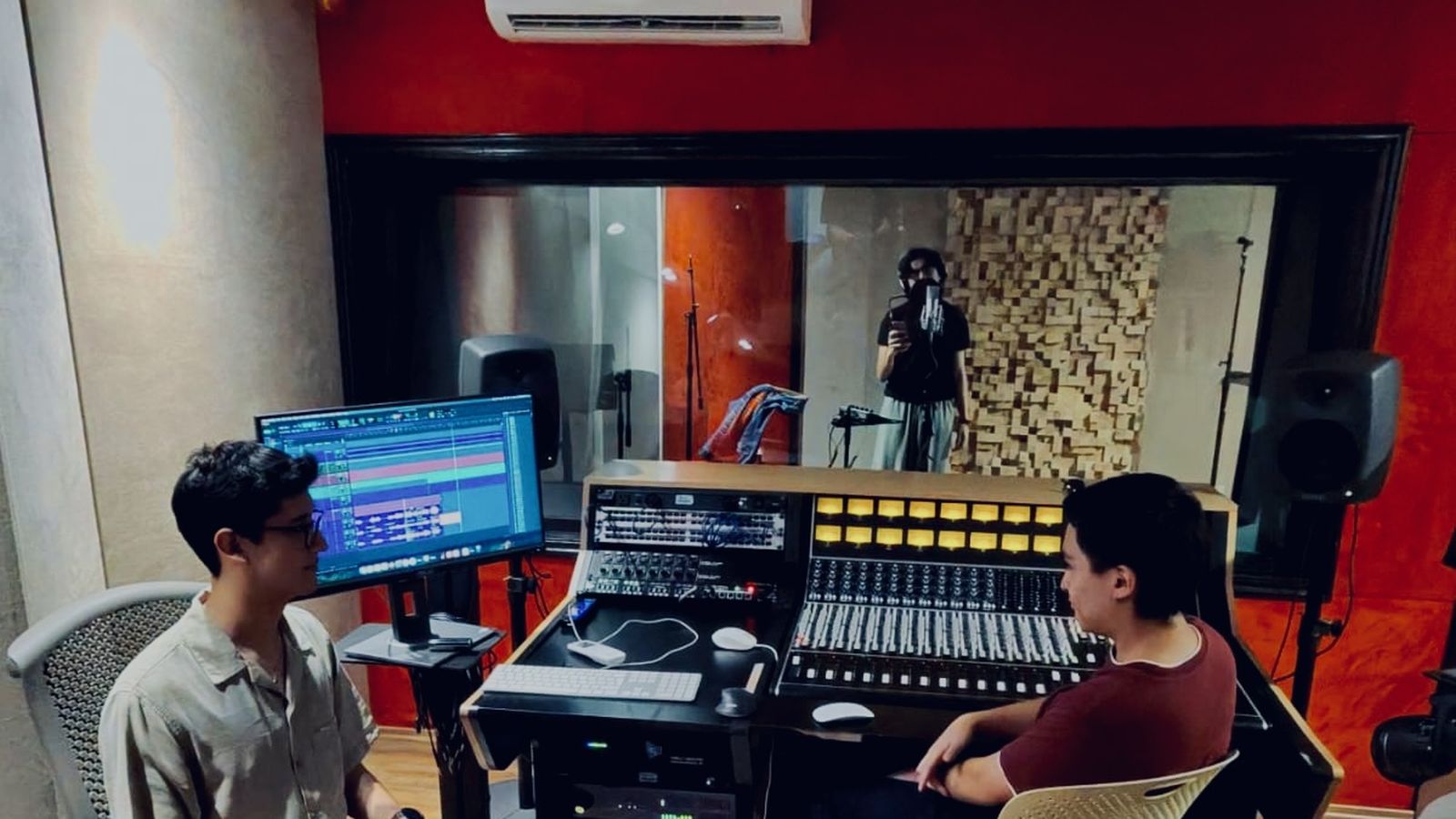 Sala de control durante una sesión con CLUB-104: dos ingenieros en la consola API y un músico grabando en la cabina.